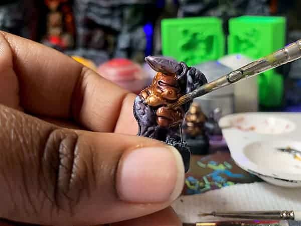 A kid painting an air-dried clay monster miniature (compare to play dough) with wargame paints in a Necromolds board game setup