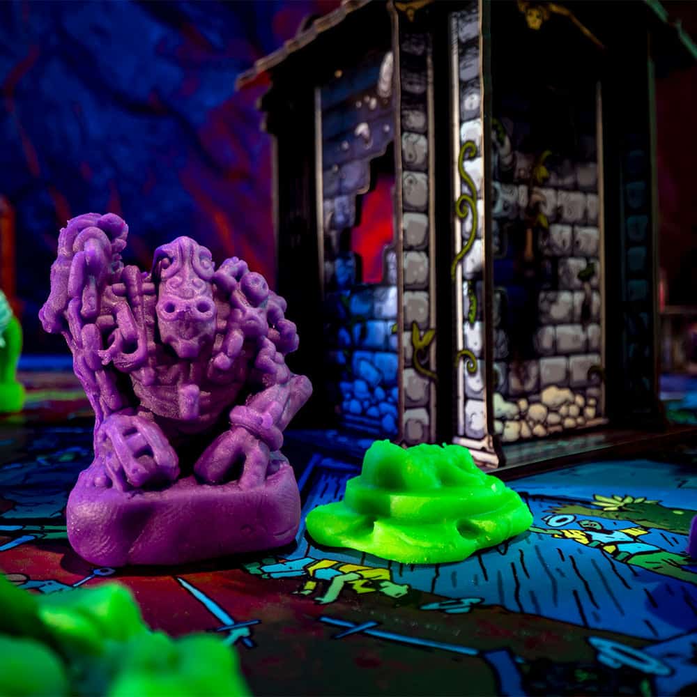 A monster miniature molded out of play doh like clay standing infront of a crypt on the board game battle map.
