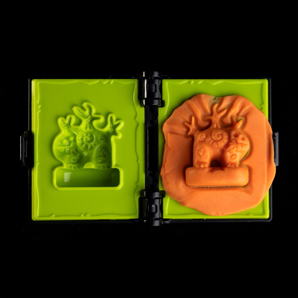 
                  
                    A spellbook shaped clay mold toy used in the Necromolds wargame to mold clay minis in the shape of creepy monsters. The clay is similar to orange play doh.
                  
                